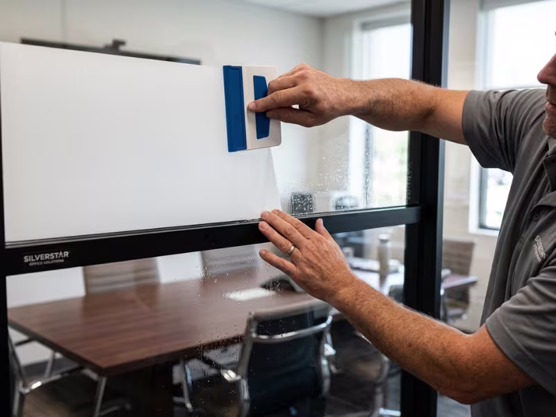 Installer applying frosted film to office glass Installer applying frosted film to office glass